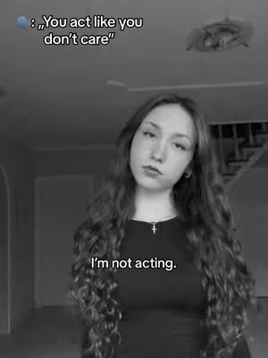 A grayscale image features a young woman with long, wavy dark hair, looking towards the camera with a somewhat serious expression. She wears a dark top and a small cross necklace. Text overlays the image, with a dialogue bubble above her head and text at the bottom.