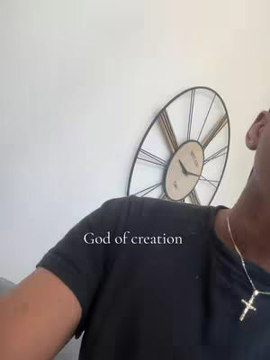 The cover image shows a man from the shoulders up in front of a white wall. A large clock with black Roman numerals hangs askew on the wall. he's wearing a black t-shirt and a cross necklace. The text overlay reads: "God of creation".
