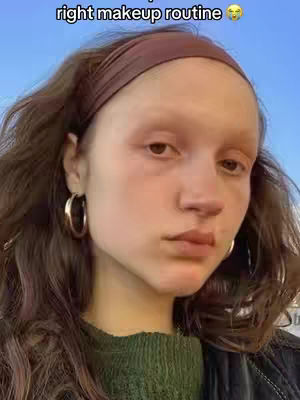 A selfie-style portrait shows a woman with long, dark brown hair and wearing a green sweater. She has a brown headband and gold hoop earrings. The background is a soft blue sky. The text "right makeup routine" appears above her head.