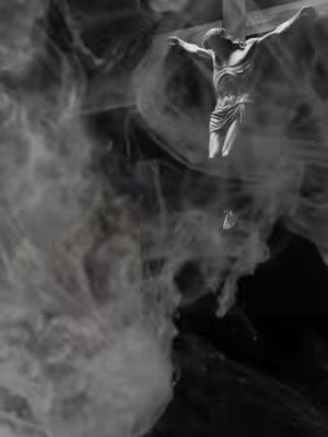A grayscale image with a dark, textured background, possibly representing smoke or clouds. In the center, a statue of Jesus Christ on a cross is visible. The statue is detailed, with visible features and clothing. The composition is dramatic, using the contrast of light and dark to highlight the figure. The overall mood is solemn and reverent.