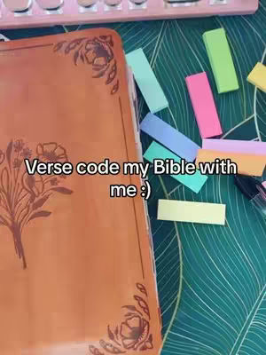 The image shows a bible open on a table with colorful sticky notes scattered around it. The bible has a floral design on the cover. The background has a green leaf pattern. Text overlay says 'Verse code my Bible with me :)'. Adjacent to the bible is a pink keyboard.