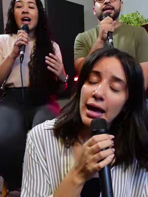 The cover image displays three individuals, two women and one man, singing into microphones. The main focus is on the woman in the foreground, with her eyes closed and mouth open as she sings. The background includes the other two people, with one woman to the left and a man to the right, also singing. The composition is a medium shot, capturing their upper bodies and the microphones. The colors are natural with the person in the bottom wearing a striped shirt.