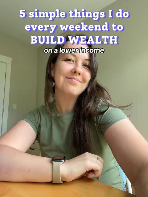 The cover image shows a woman sitting at a table, looking at the camera with a slight smile. Text overlayed on the image reads, '5 simple things I do every weekend to BUILD WEALTH on a lower income.' The woman is wearing a green t-shirt, a watch, and a ring. The background is a room with a neutral wall and a cabinet is partially visible.