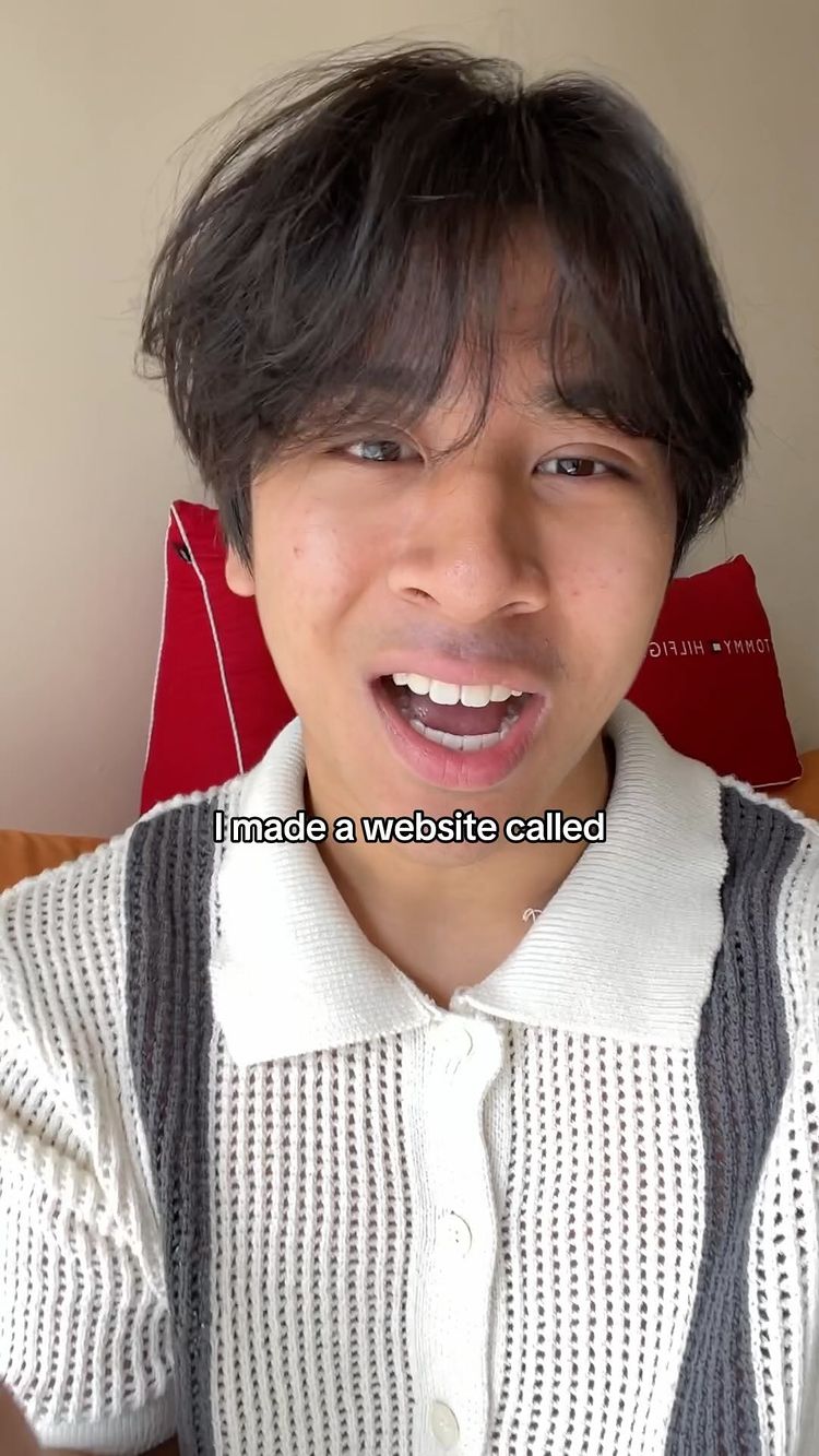 A young man with short, dark hair is centered in the frame, looking directly at the camera with a surprised expression. He wears a white and gray striped sweater. Behind him, a red pillow is visible. Text overlay reads, "I made a website called."