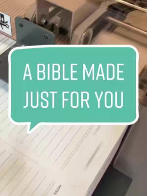 Image showing machinery constructing a spiral-bound notebook bible. The hook features a teal speech bubble with white text.