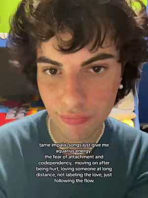 A selfie style shot featuring a young person with brown curly hair, a blue shirt, and a pearl necklace. The person is looking directly at the camera with a slight smile. Overlayed on the image is text related to Aquarius energy.