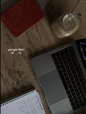 An overhead shot shows a wooden desk with a red textured pad, a notebook with handwriting, a laptop, and a glass of what appears to be a latte with a spoon in it. The words 'you got this!' are overlaid on the image in a handwritten font.