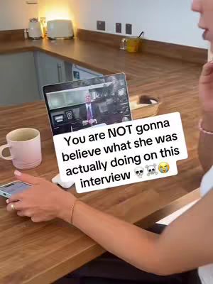 A person's arm and hand are visible, resting on a wooden surface. They are holding a phone in their left hand and there's a laptop displaying a screen to the side. A white text box sits on top of the laptop image.