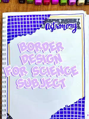 A notebook page with a border design for the science subject, featuring the words 'BORDER DESIGN FOR SCIENCE SUBJECT' in a highlighted font, along with an 'Astronomy' title, a grid border, and a collection of colored markers in the background.
