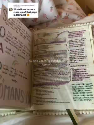 The image shows an open book, likely a Bible, with handwritten notes and highlighted passages. The book is open to two pages, with text and annotations covering both. The left page has larger, more stylized lettering with highlighted words and phrases. The right page is densely filled with smaller text, also highlighted, and includes arrows and connecting lines. The pages are on a bed covered by a floral-patterned blanket.