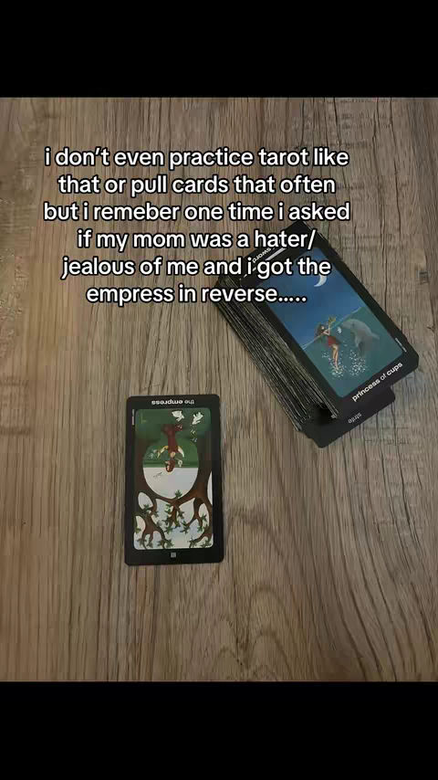 The image shows a wooden surface with two tarot cards in view, one upright and one upside down, along with a deck of cards tilted in the upper right, all arranged for a reading.