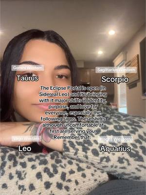 A woman is leaning on her arms, with text overlays indicating various zodiac signs and a central message about an eclipse. The image has a warm indoor lighting and a blurred background.