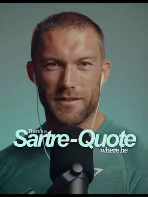 A man with short hair and a beard looks at the camera, wearing a green shirt and earbuds. A microphone is positioned in front of him with text overlaying the bottom, which is a teal-colored background.