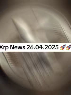 A blurry, abstract image featuring a central shape that could be a coin or metallic object. Overlayed in a white rectangular bar is black text with the words "Xrp News 26.04.2025" and two rocket emojis. The background has a blurred effect, which may be due to a camera effect or the original environment.