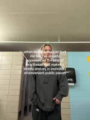 A woman in a grey hoodie and black pants stands in a public restroom, positioned slightly off-center. Text overlays captioning her experience on the top of the cover.