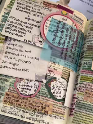An open book with handwritten notes and colorful sticky notes, a variety of sizes and shapes. The pages have text from the bible. The notes are attached to the page with tape.