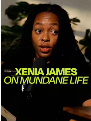 A woman with long black hair sits in front of a dark background. The text overlay reads "XENIA JAMES ON MUNDANE LIFE" in a vibrant, green color. A microphone is positioned in front of her. The color palette includes dark greens and blacks, with the bright green text providing a focal point.