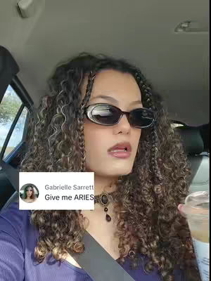 A selfie taken in a car. The creator is wearing sunglasses, has curly hair, and a purple shirt. A text box with the creator's name and the phrase 'Give Me ARIES' is on the lower left.
