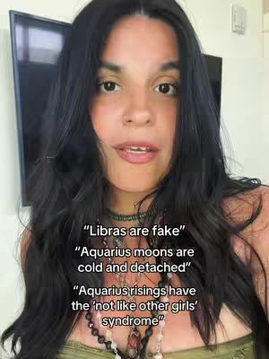 A woman with dark hair and fair skin is centered in the frame, looking towards the camera against a blurry background. She is wearing a green top and multiple necklaces. Text overlays appear on the image describing zodiac signs.