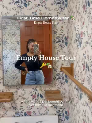 The video cover is a mirror selfie taken in what appears to be a bathroom. The room features wallpaper with a floral pattern and a wooden door. The person is standing in front of a mirror, holding the phone to take the picture. The text overlay says 'First Time Homeowner' and 'Empty House Tour'. The background setting is of a room with floral wallpaper and wooden trim and door.