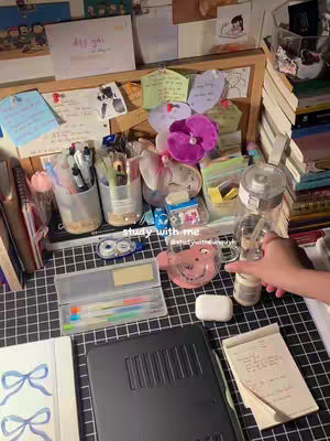 The image shows a desk setup with study materials such as notebooks, pens, sticky notes, and a water bottle. The main focus is on the items relevant to studying, giving a sense of organized productivity.