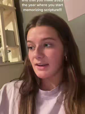 A woman with long brown hair speaks directly to the camera, set against a softly lit background including a shelf and window.