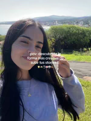 A young woman with long dark hair smiles while looking at the viewer, an outdoor nature scene blurred in the background. Text is overlaid on the image with the words 'pov: descubriste la forma más creativa de subir tus stories !'. Overall, the image is bright and captures a candid, natural moment.