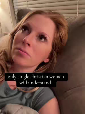 A woman with fair skin and reddish-blonde hair looks upward with a thoughtful expression. She is laying on a brown couch. The image has a warm, slightly dim lighting.