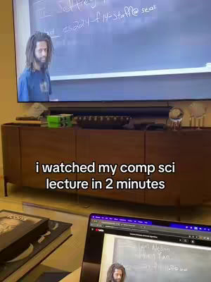 A man with long hair stands against a large TV screen with text on it. The text "i watched my comp sci lecture in 2 minutes" is overlaid on the cabinet below the TV. A laptop displaying content is in the bottom right corner.