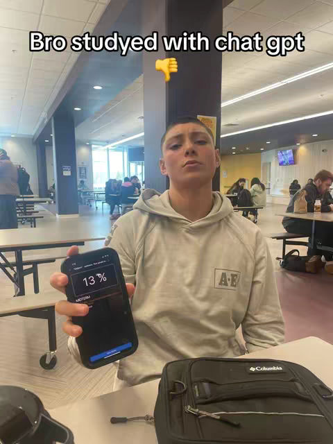 A young man in a hoodie holds up a smartphone, displaying 13% and the word 'MIDTERM'. He is in a cafeteria setting with tables and other people visible in the background.
