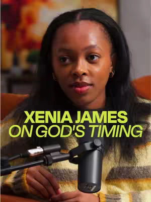 A woman with dark hair and wearing a yellow sweater is positioned in front of a microphone. The background is blurred, showing hints of an abstract painting and a plant. Text overlayed on the image reads "XENIA JAMES ON GOD'S TIMING", written in a green-yellow font.