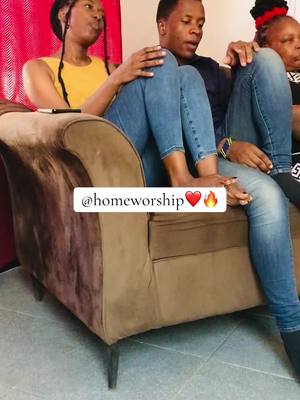 The cover image shows a candid shot of three people, seemingly indoors, seated on a brown couch. A woman with black braids is seated on the left, wearing a yellow top. A man sits in the middle, wearing a dark shirt and blue jeans, with his bare feet up. Another woman is seated to the right. Text overlaid on the image reads '@homeworship', along with heart and fire emojis.