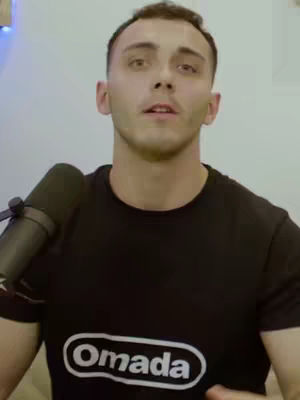 A man in a black t-shirt with the word 'Omada' on it is looking up at the camera with a microphone in the frame. Soft lighting creates a natural look.