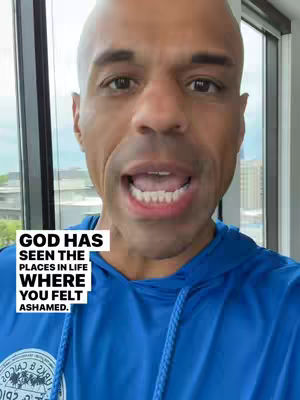 A man with a shaved head and open mouth speaks directly to the camera, with additional overlaid text. He wears a blue hoodie.