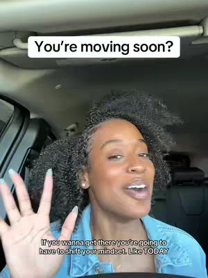 A woman with curly hair is sitting in a car and looking directly at the camera with a smile. She has her hand up, with her fingers spread out. The background shows the car’s interior.
