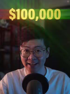A man with glasses is smiling, with text overlayed above his head. The text is in a yellow, stylized font. The background has blurred, colorful gradients. A black microphone is in front of him.