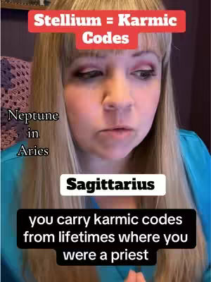 A medium shot features a woman centered in the frame. She has long, light brown hair with bangs and is wearing a blue top. Text overlays are above, below, and to the left of her, describing “Stellium = Karmic Codes”, “Neptune in Aries”, and “Sagittarius”, as well as a description, “You carry karmic codes from lifetimes where you were a priest”.