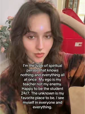A woman with long, wavy brown hair looks directly at the camera. She is wearing a dark, tie-dye style shirt, and a small nose ring can be seen. Overlayed on the image is a block of text in a white, sans-serif font.