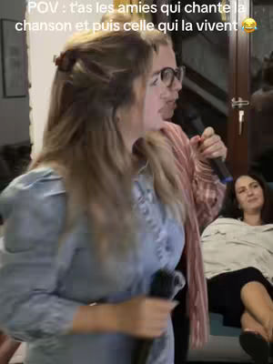 The image showcases a woman holding a microphone, central to the shot, poised as if singing or speaking at a karaoke event. The background subtly reveals other individuals, likely the other friends or attendees of the karaoke. The lighting gives the image an indoor look.