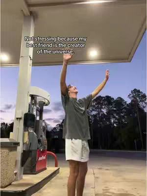 A man stands outdoors with his arms raised towards the sky, under the canopy of a gas station. He wears a gray t-shirt and white shorts. Text is overlaid.