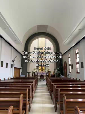 An interior shot of a church or chapel. The camera is positioned at the back, looking towards the altar, which is located at the end of a long aisle lined with rows of wooden pews on either side. The space is brightly lit, with arched ceilings and large windows. A text overlay is present at the top center.