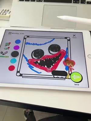 A tablet screen displaying a drawing of the Huggy Wuggy character from Poppy Playtime. The drawing is in a whiteboard style, with simple outlines filled in with color. The background includes parts of a laptop, a stylus, and a keyboard.