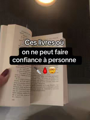 An open book with text at the center, a hand with reddish nails touches the left page, and a text overlay highlights the books. Above is a light. The text box has the words "Ces livres où" and the text on line below reads "on ne peut faire confiance à personne". Below the text, are emojis of a knife, a drop of blood, and a face with confused eyes.