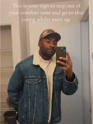A man in a denim jacket and camo hat takes a selfie in a bathroom mirror. Text overlays encourage viewers to step out of their comfort zone and attend a young adults meetup.