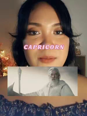 A woman with dark hair and makeup is centered in the frame. A text overlay 'CAPRICORN' in a pink gradient font hovers over her face. Below her is an image of a man with long white hair and beard, holding a staff, likely from the Lord of the Rings series. The background is blurred, with warm tones suggesting indoor lighting.