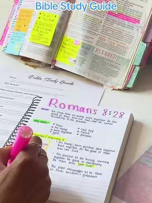 The image shows an open bible and a handwritten notebook next to it. The bible has sticky notes and tabs in multiple colors, and highlighted text. The notebook has notes about a bible study with a pink highlighter