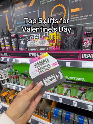 The cover image shows a person's hand holding a package of Muc-Off Tubeless Rim Tape, set against a backdrop of store shelves stocked with various bike-related products. The top of the image features text that reads 'Top 5 gifts for Valentine's Day.'