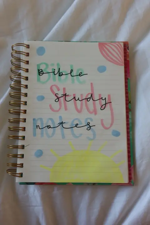 A notebook with Bible study notes is seen on a white blanket. The notebook is open and the text overlay says Bible, study, and notes.