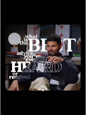 A man in a dark buttoned shirt is seated in a well-lit room. Overlaid on the scene is stylized white text asking "what is the BEST advice you've ever or received." A soft white light shines to the left of the man, and in the background, a blurred image of a sign and other objects offer a sense of a comfortable interior. The man is looking forward and wearing a warm smile.