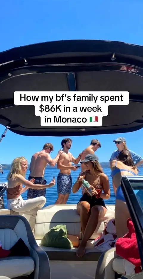 A group of people are on a boat on a sunny day. Text in a white rectangle at the top of the frame reads, "How my bf's family spent $86K in a week in Monaco." The group includes people of various genders and ethnicities; some are shirtless. The people are casually interacting, with drinks in hand.